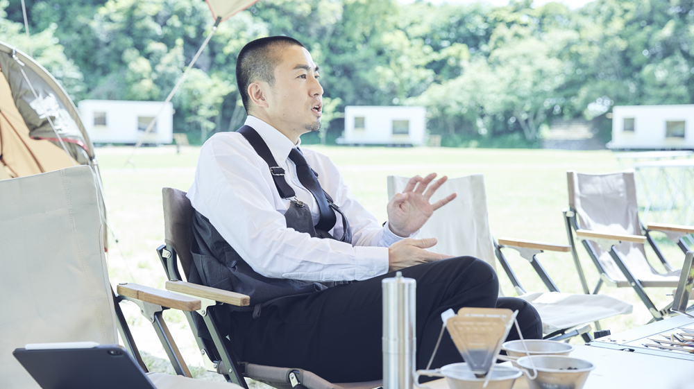 フォーマルな装いにキャンプ用の「タキビベスト」をまとった上山氏。装いからもアウトドアに新風を吹き込む