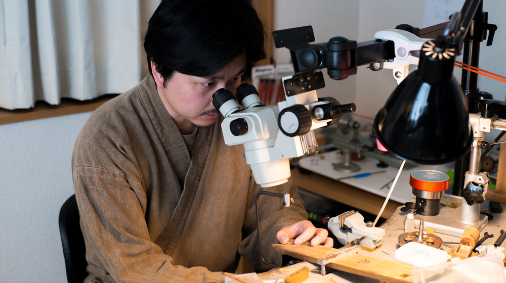 文字盤を製作中の菊野氏。顕微鏡を覗きながら糸ノコを使って手作業で文字盤を加工していく
